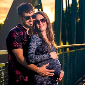 Ein liebevolles Paar im Abendlicht auf einer Bruecke am Maschsee. Die werdende Mutter haelt sanft ihren Babybauch im Arm.