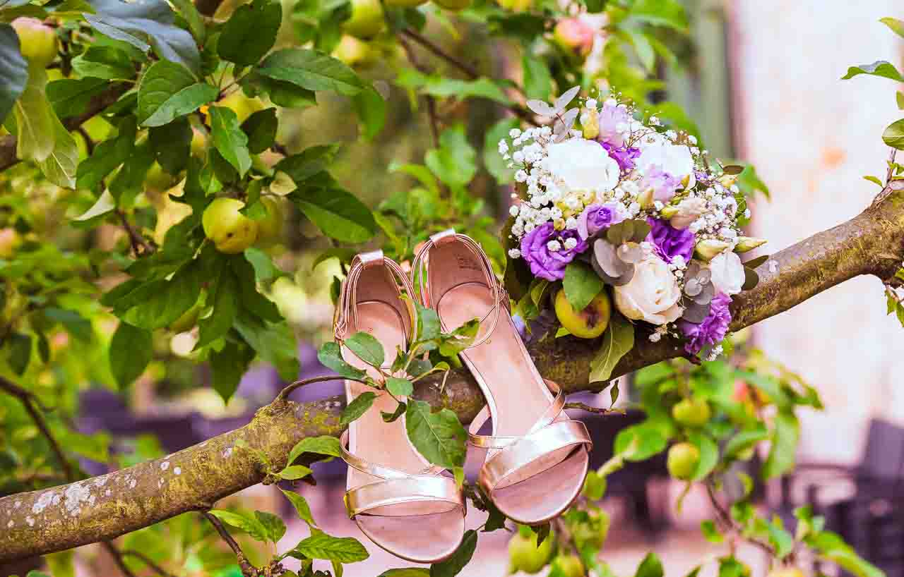 Brautschuhe und Blumenstrauß auf Apfelbaum-Ast. Romantische Hochzeit in Mosterei Ockensen. Zarte Details für die Braut.