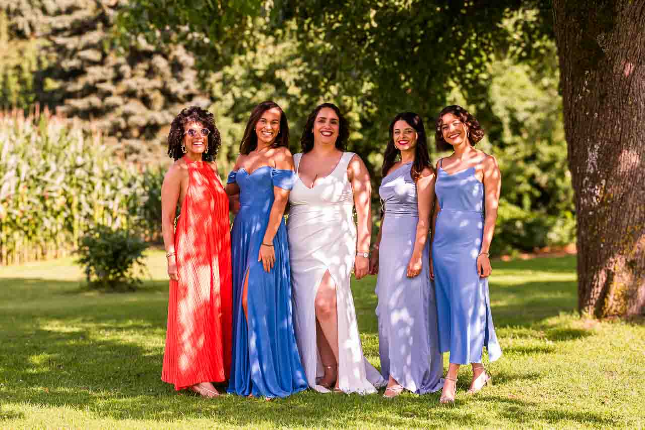 Braut mit Brautjungfern in farbenfrohen Kleidern im Garten. Elegante Hochzeitsgesellschaft strahlt sommerliche Fröhlichkeit aus.