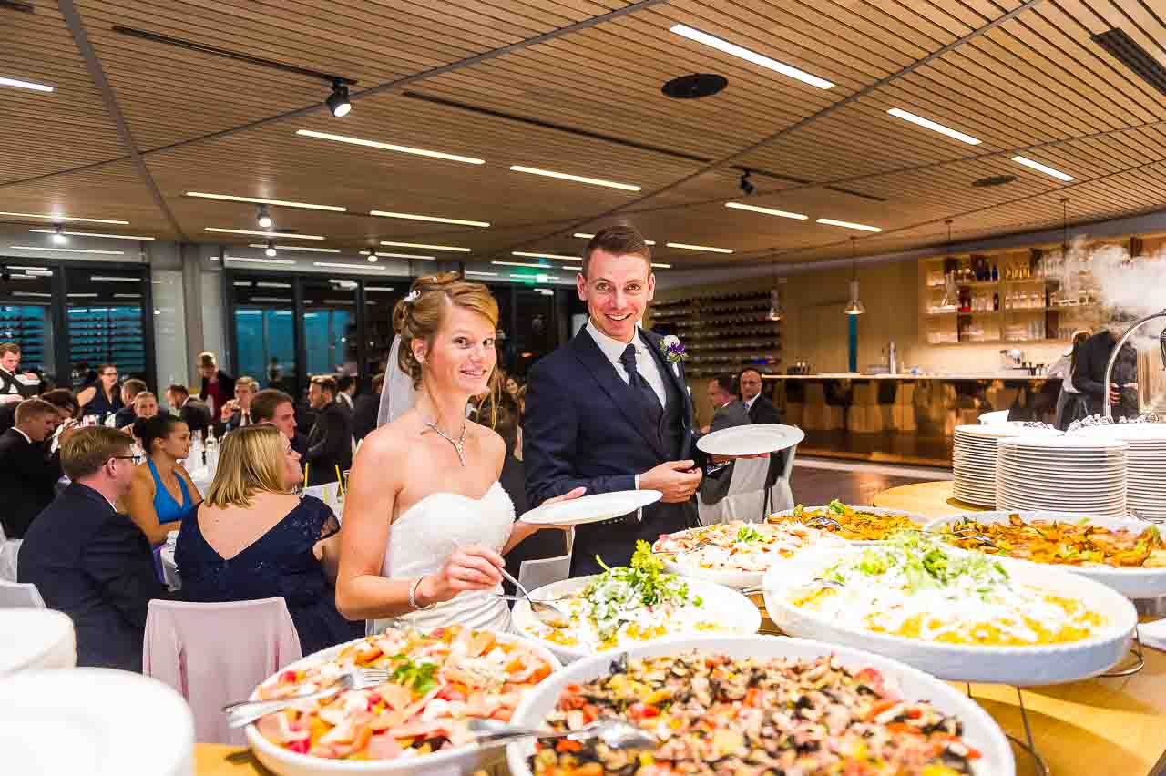 Ein strahlendes Brautpaar am Buffet, die Braut in Weiss, der Braeutigam im dunklen Anzug. Liebevolle Details und festliche Atmosphaere im Blick.