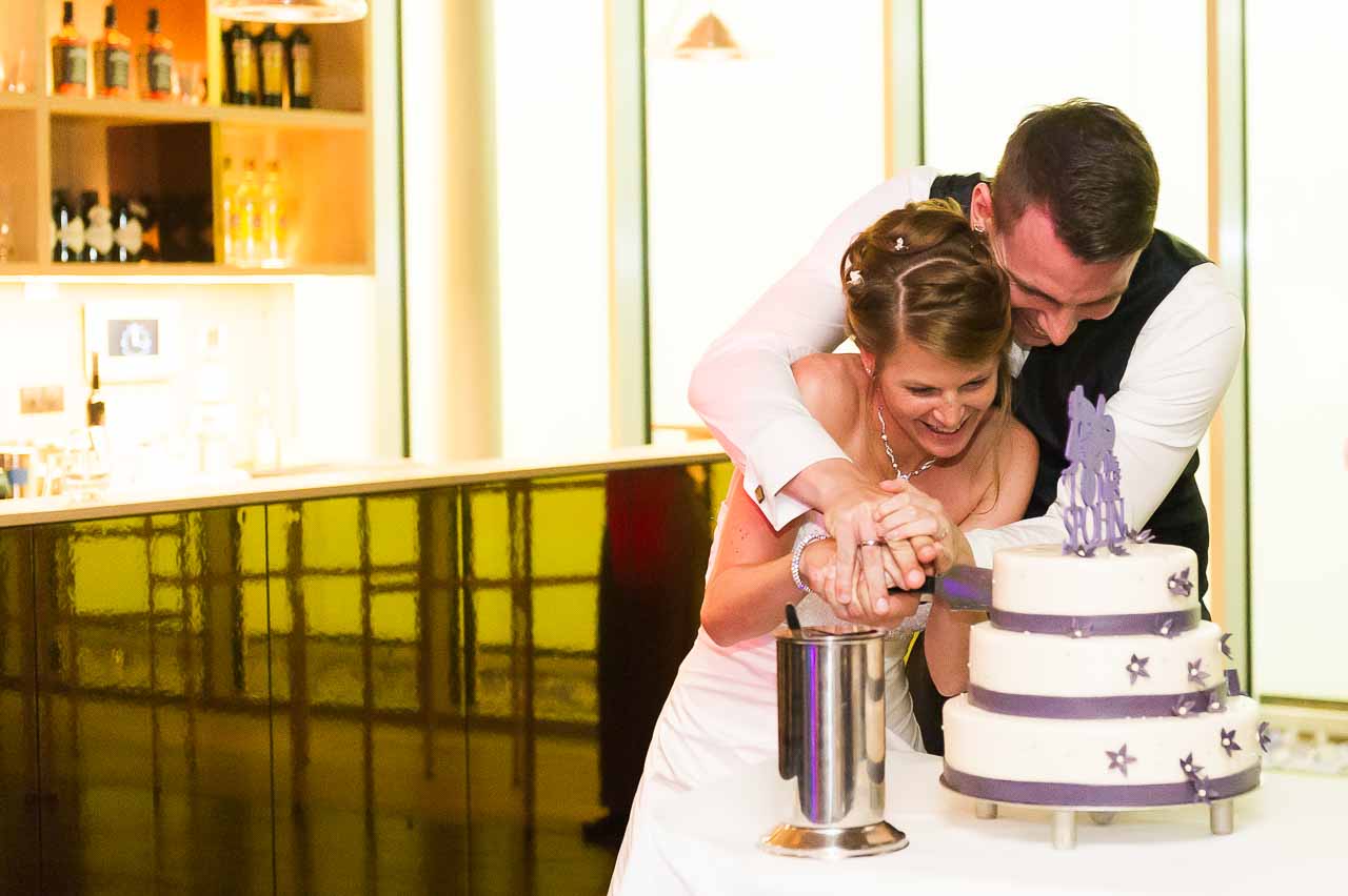 Ein strahlendes Brautpaar schneidet gemeinsam die Hochzeitstorte an. Die Atmosphaere ist voller Freude und Zuneigung, ein unvergesslicher Moment.