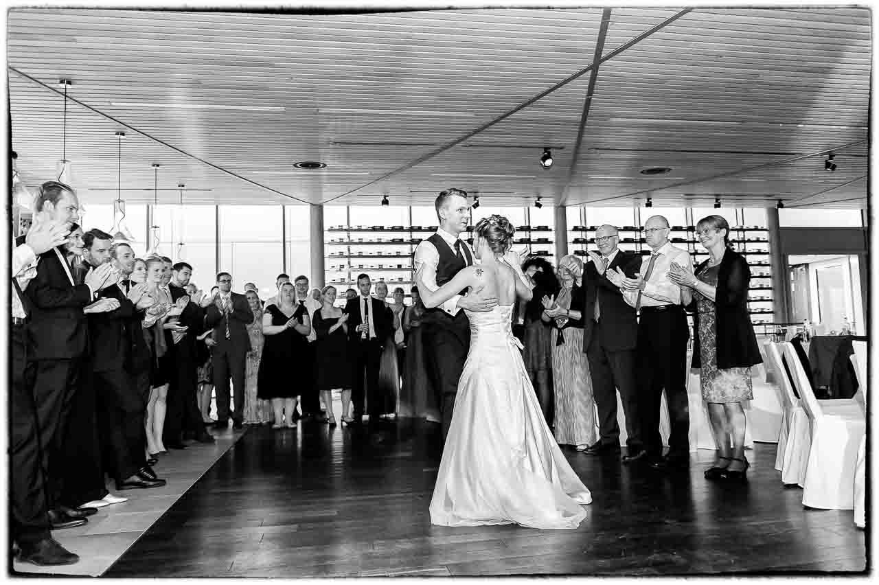 Ein Brautpaar tanzt innig, umgeben von applaudierenden Gaesten. Die Atmosphaere ist festlich und romantisch. Ein unvergesslicher Moment einer Hochzeit.