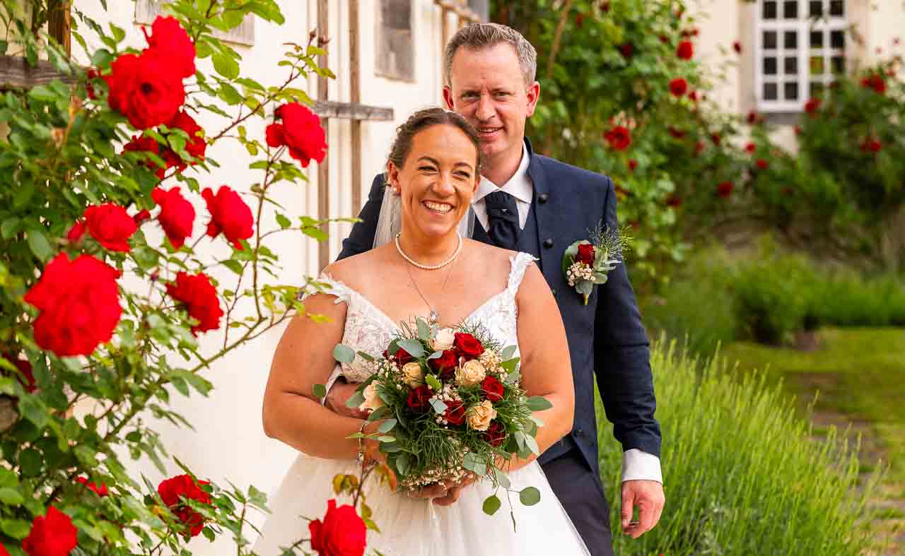 Romantische Hochzeit: Braut mit Rosenstrauss und Braeutigam vor Schlosskulisse. Das Glueck strahlt in ihren Augen, ein unvergesslicher Tag im Schloss.