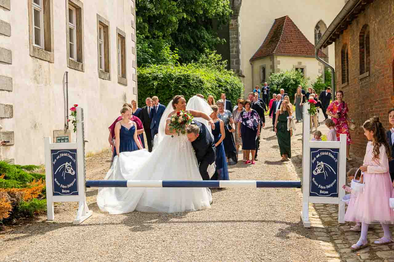 Romantische Hochzeit: Brautpaar schreitet unter Ehrenbogen hindurch, begleitet von festlichen Gaesten. Liebevolle Details und strahlende Freude im Schloss.