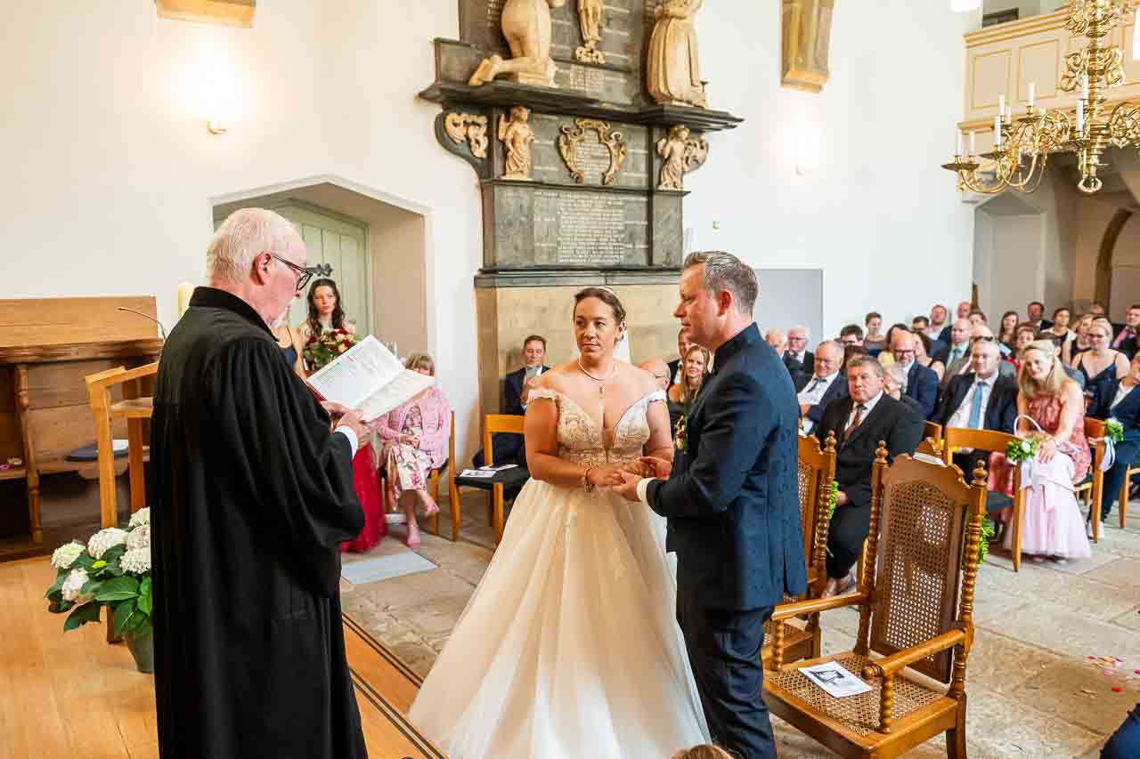 Kirchliche Trauung: Brautpaar im eleganten Brautkleid und dunklem Anzug gibt sich in der Kirche das Ja-Wort, umgeben von Gästen.