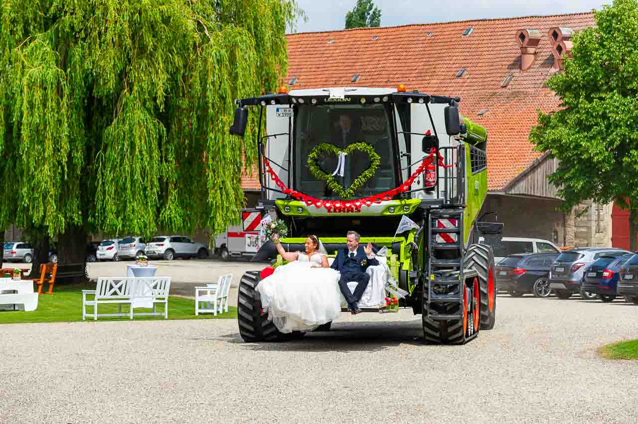 Hochzeit einmal anders: Brautpaar auf einem geschmueckten Maehdrescher. Das Herz aus Gruen und die rote Schleife sind ein echter Hingucker.