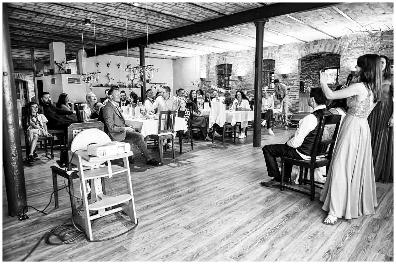 Stilvolle Hochzeitsfeier in Mosterei Ockensen: Festlich gedeckte Tische, elegante Gäste und eine anmutige Rednerin. Romantische Atmosphäre.