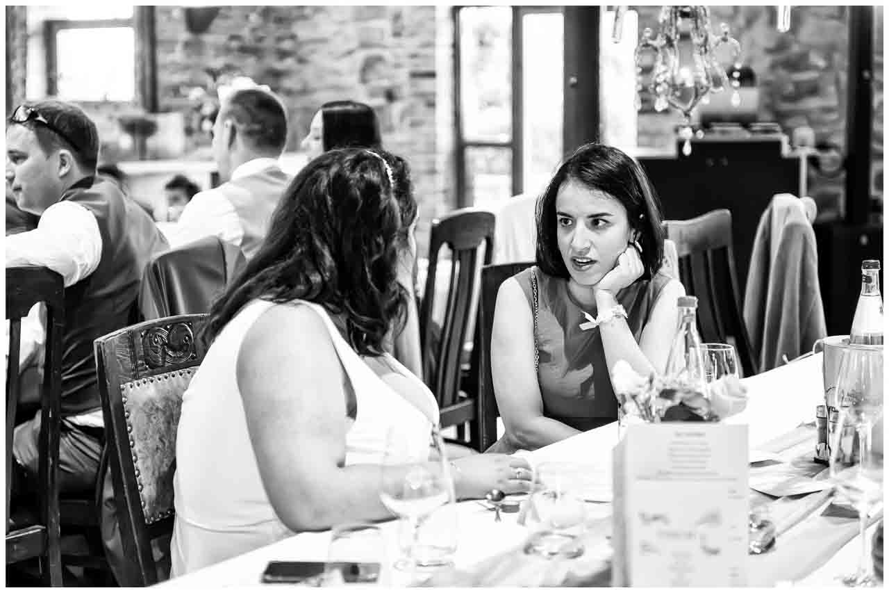 Festliche Hochzeitsgesellschaft in Ockensen: Zwei Frauen im Gespräch an der elegant gedeckten Tafel. Stilvolle Feier in Schwarzweiß.