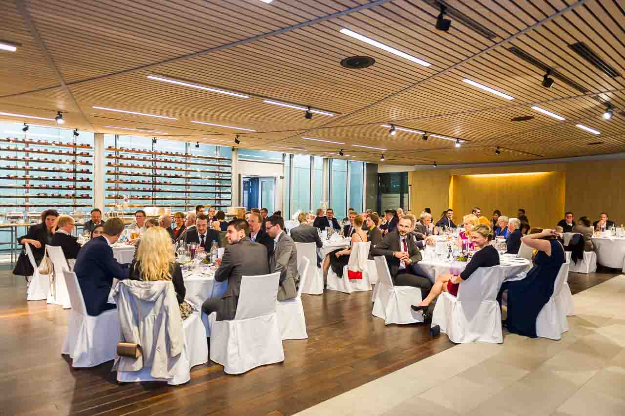 Elegante Hochzeitsgesellschaft sitzt an festlich gedeckten Tischen. Die Atmosphaere ist feierlich, die Dekoration stilvoll und einladend fuer das Brautpaar.