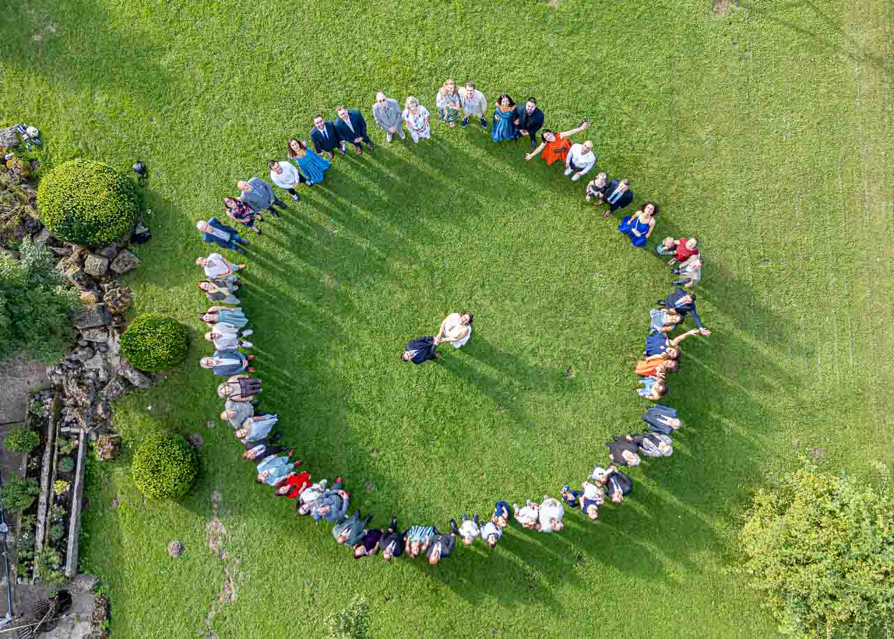 Luftaufnahme: Menschen bilden Kreis um Brautpaar auf Rasen in Mosterei Ockensen. Festliche Hochzeitsgesellschaft, idyllische Szene.