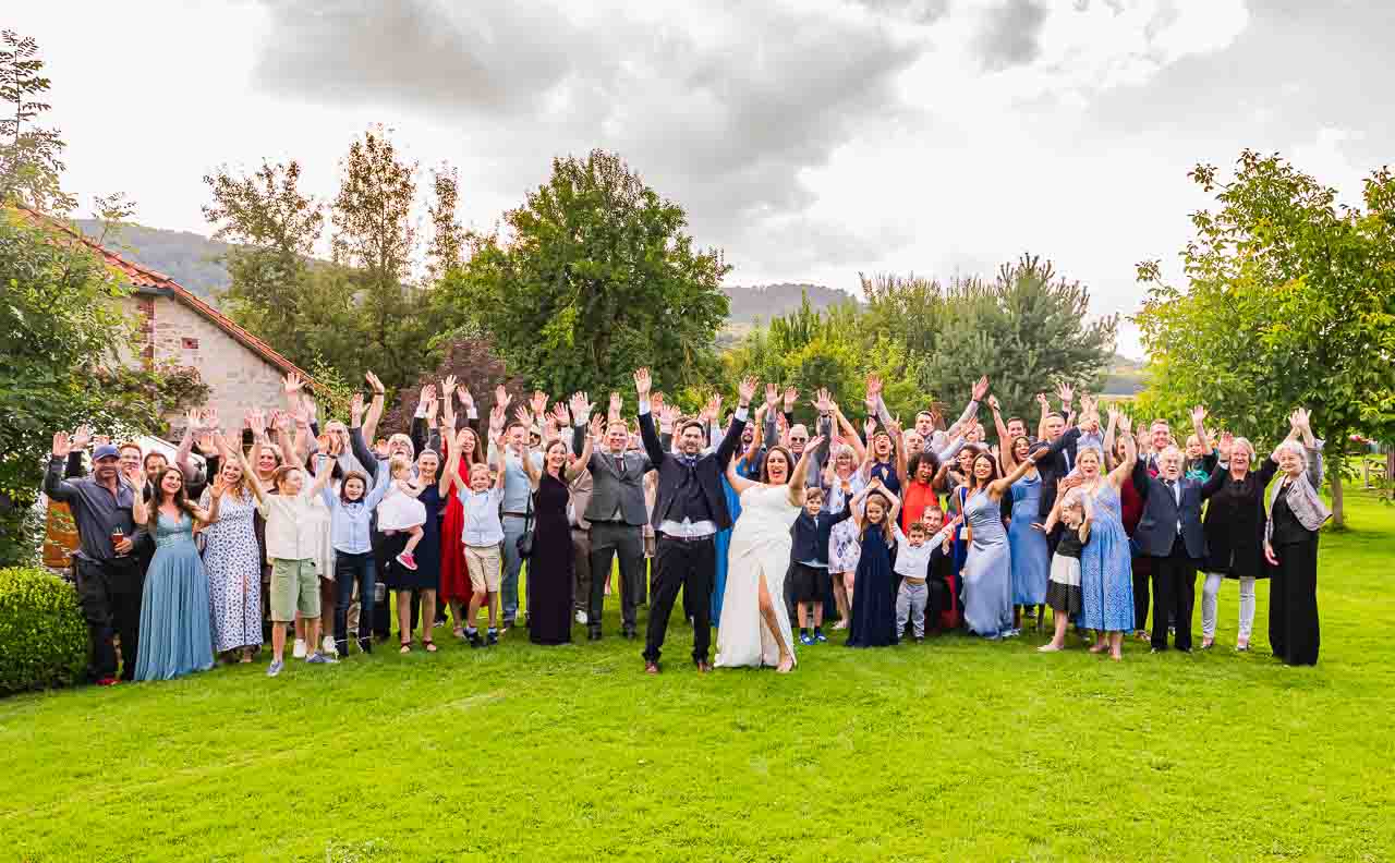 Hochzeitsgesellschaft feiert ausgelassen im Grünen. Die Braut strahlt in ihrem Kleid, umgeben von Familie und Freunden. Unvergessliche Momente.