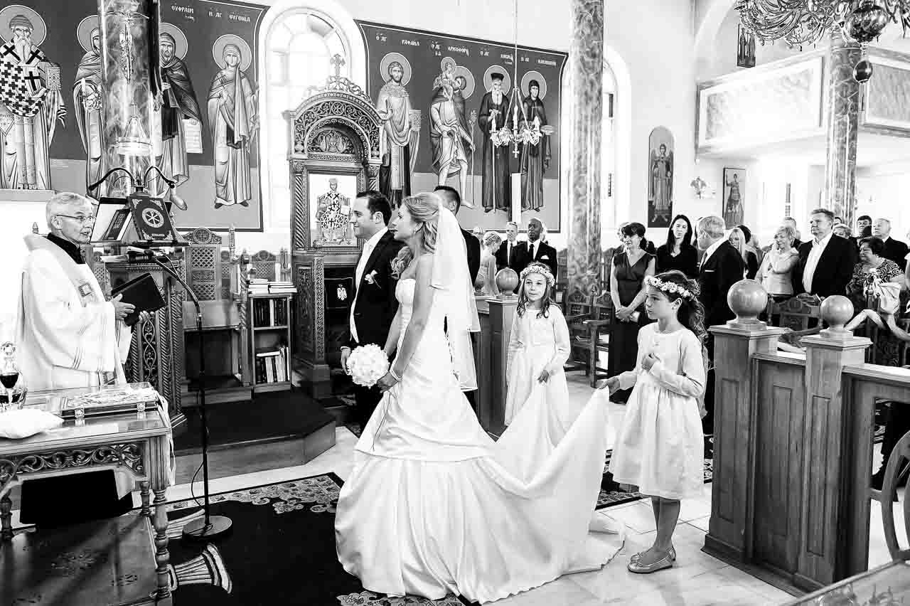 Stilvolle Hochzeitszeremonie in der Kirche: Die Braut, begleitet von Blumenmaedchen, schreitet zum Altar, wo der Braeutigam und der Priester warten.