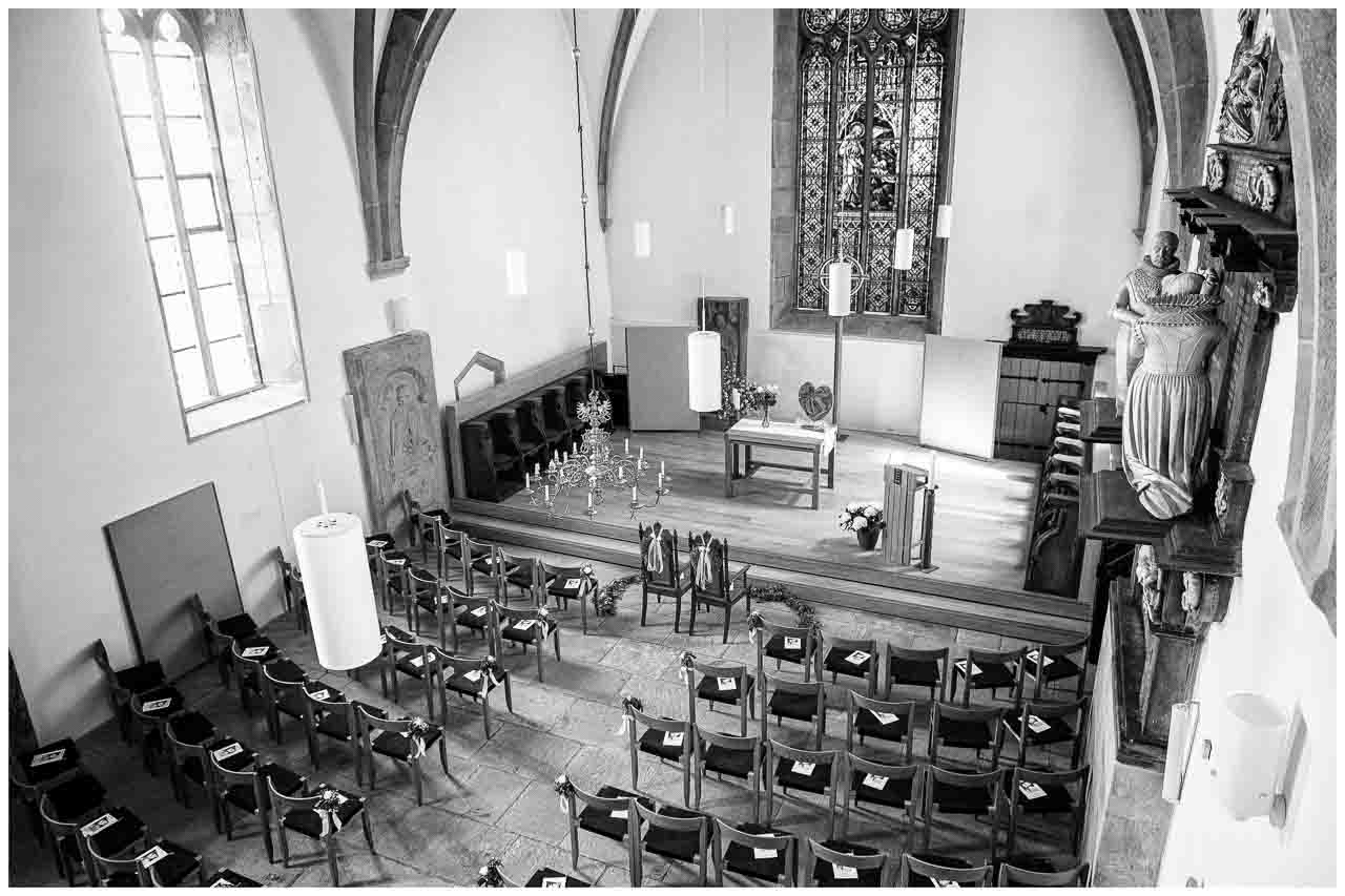Elegante Hochzeitsdekoration in der Kirche: Blick auf den Altar, geschmueckte Stuehle und das sanfte Licht durch das Buntglasfenster. Festliche Atmosphaere.