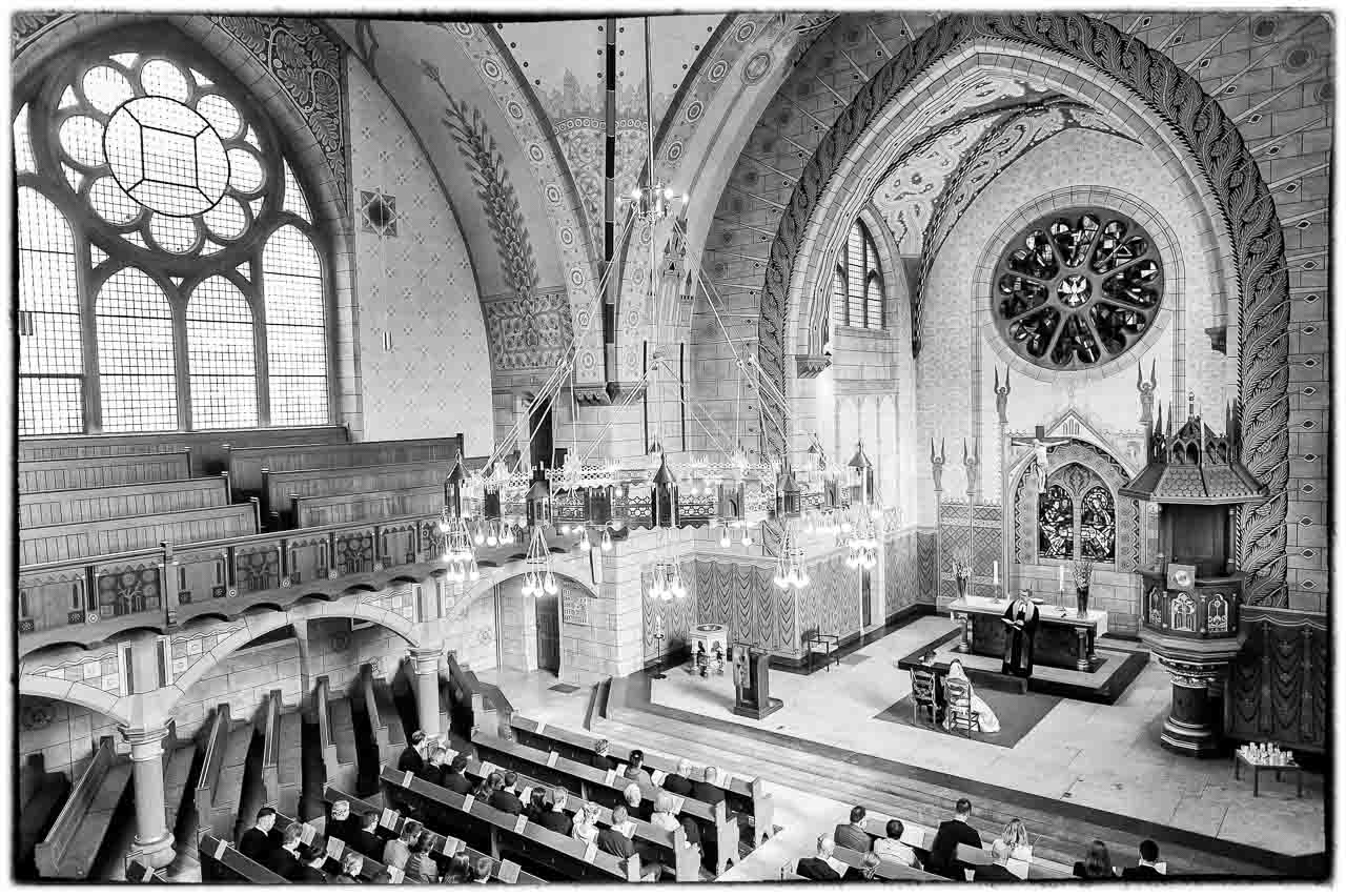 Elegante Hochzeitszeremonie in einer historischen Kirche: Das Brautpaar gibt sich das Ja-Wort vor dem Altar, umgeben von festlicher Atmosphaere.