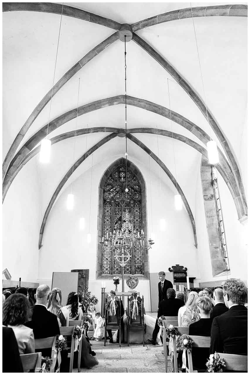 Feierliche Hochzeitszeremonie in der Kirche: Brautpaar vor dem Altar, umgeben von Gaesten. Elegante Atmosphaere, schoene Dekorationen.