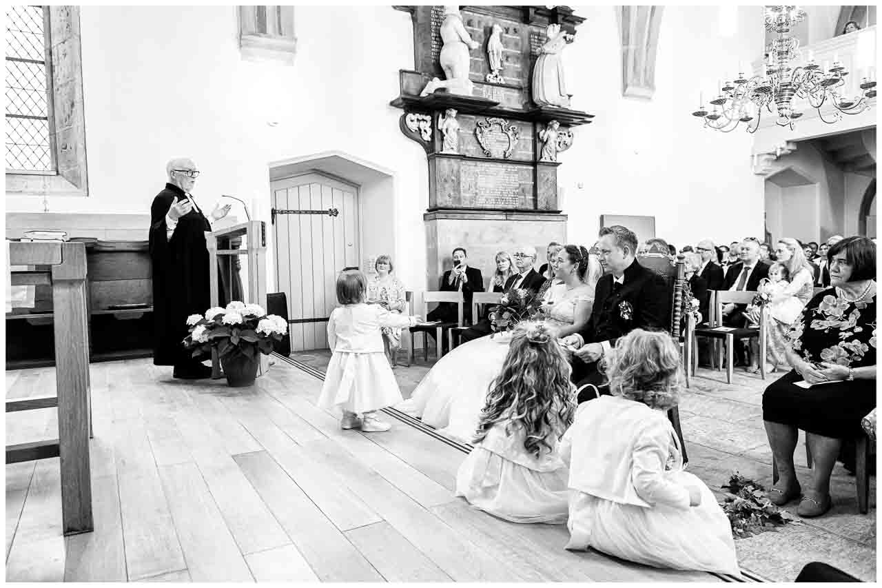 Kirchliche Hochzeit: Brautpaar sitzt andächtig, während ein Pfarrer spricht. Blumenmaedchen verzaubern die Zeremonie in der Kirche. Festlicher Moment.