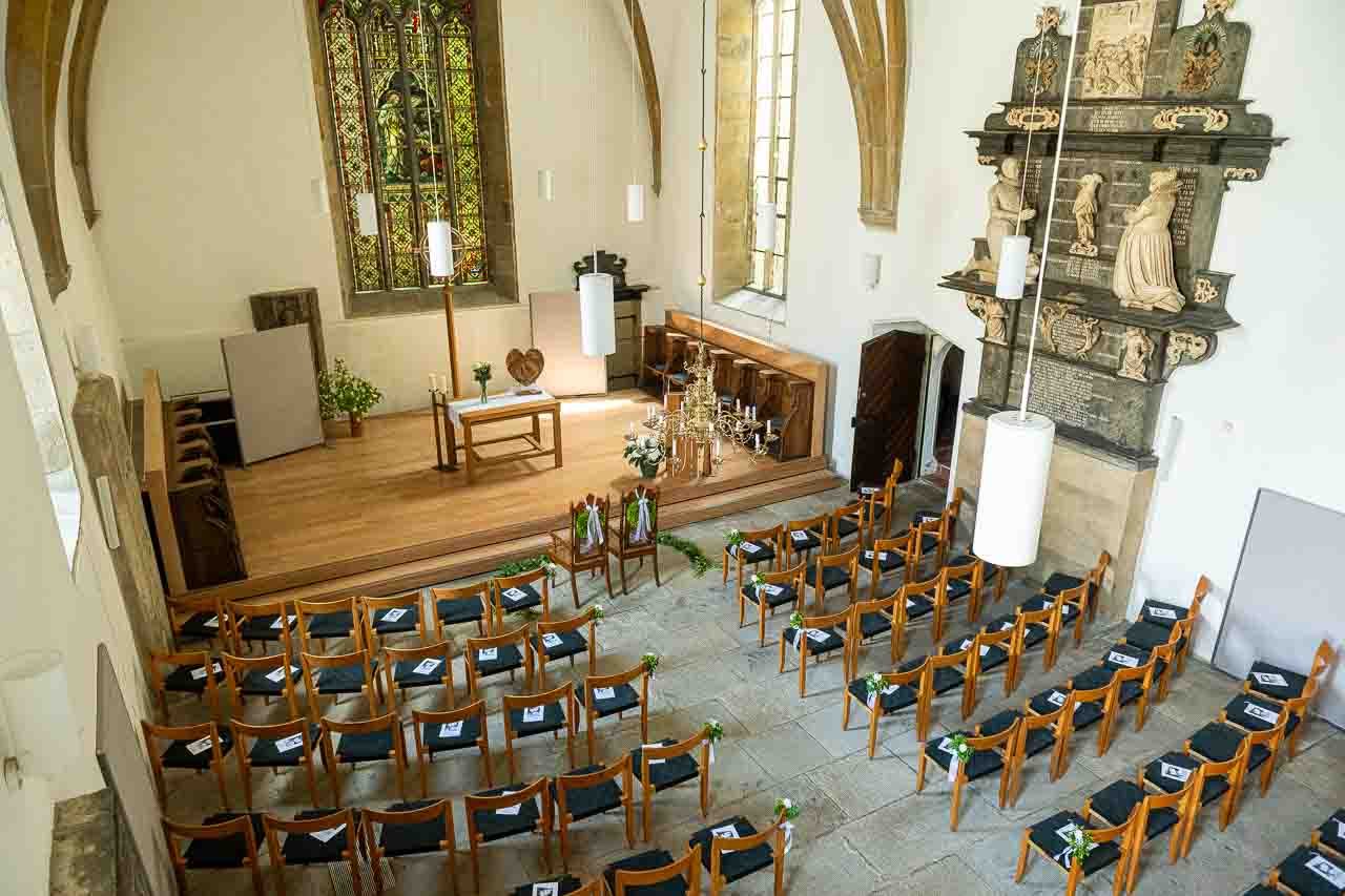 Festliche Hochzeitsdekoration in der Kirche: Holzstuehle mit zarten Blumen geschmueckt, einladende Atmosphaere fuer den besonderen Tag.