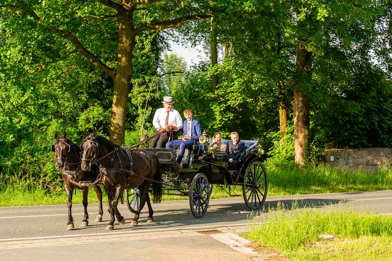 Romantische Hochzeitskutsche mit Brautpaar auf dem Weg zur Trauung. Die elegante Fahrt durch die Natur verspricht einen unvergesslichen Hochzeitstag.