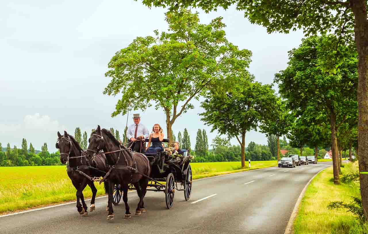 Romantische Hochzeitsfahrt: Brautpaar in eleganter Kutsche mit zwei schwarzen Pferden auf dem Landweg. Eine schoene Erinnerung an den Hochzeitstag.