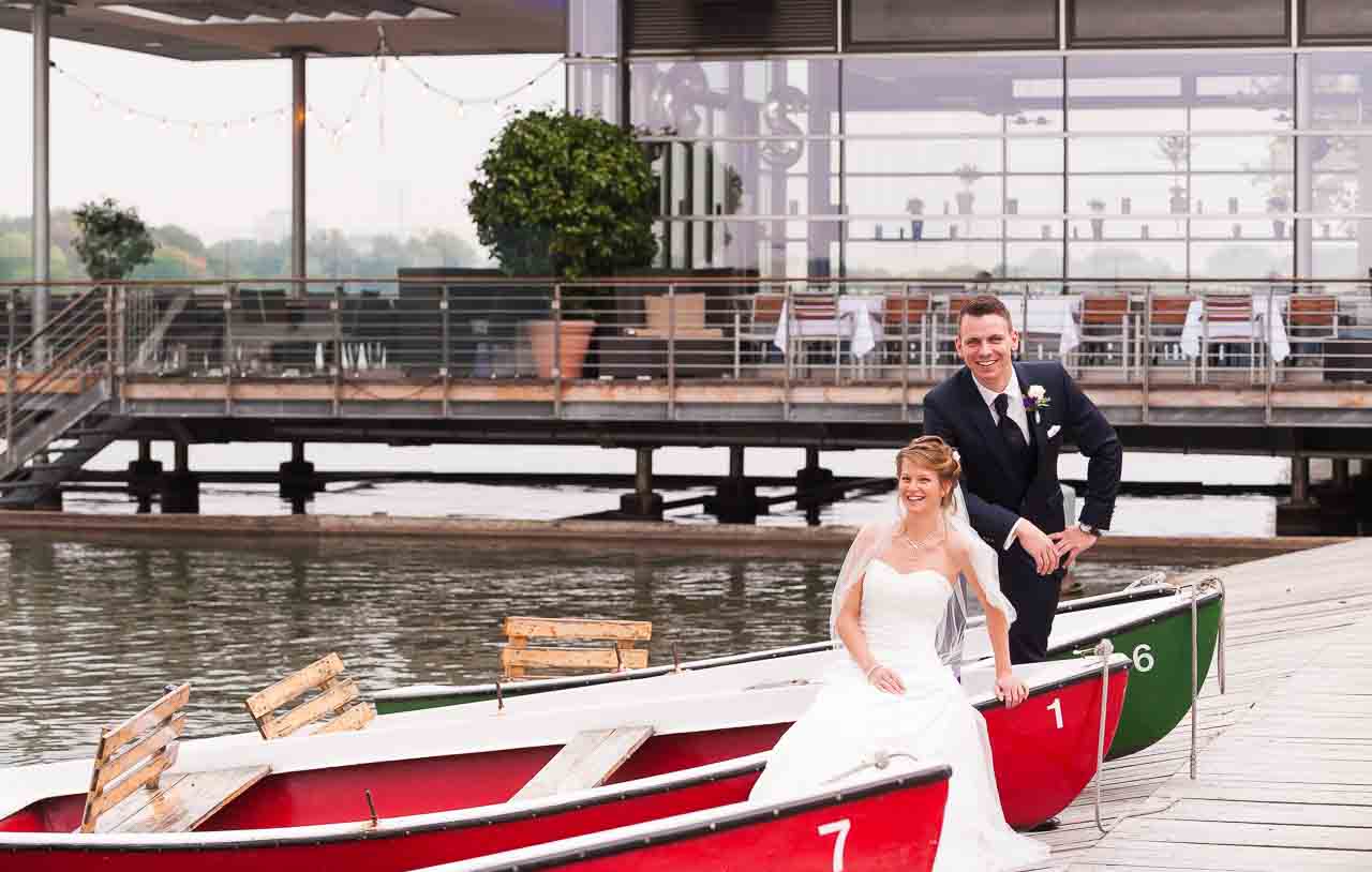 Ein strahlendes Brautpaar am Maschsee, vertraeumt in roten Ruderbooten. Die Braut, elegant im weissen Kleid, der Braeutigam im dunklen Anzug.