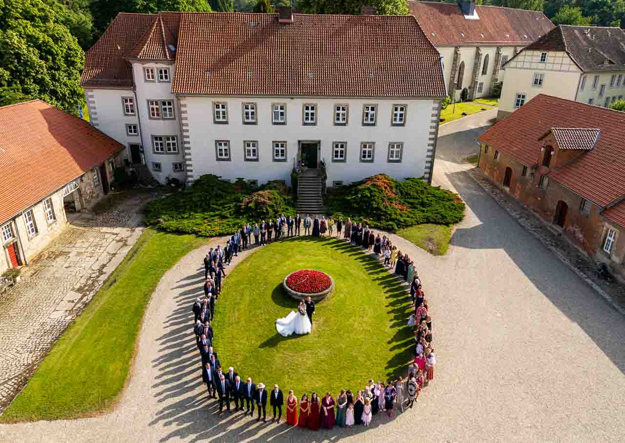 Hochzeitsgesellschaft im Schlossgarten: Brautpaar umringt von Gaesten, ein unvergesslicher Moment vor historischer Kulisse. Festliche Atmosphaere.