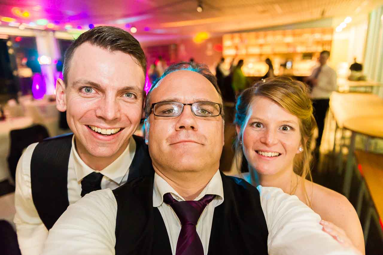 Ein strahlendes Laecheln faengt den Zauber ein: Braeutigam, Braut und ein Gast halten den besonderen Tag mit einem Selfie fest. Die Atmosphaere ist festlich.