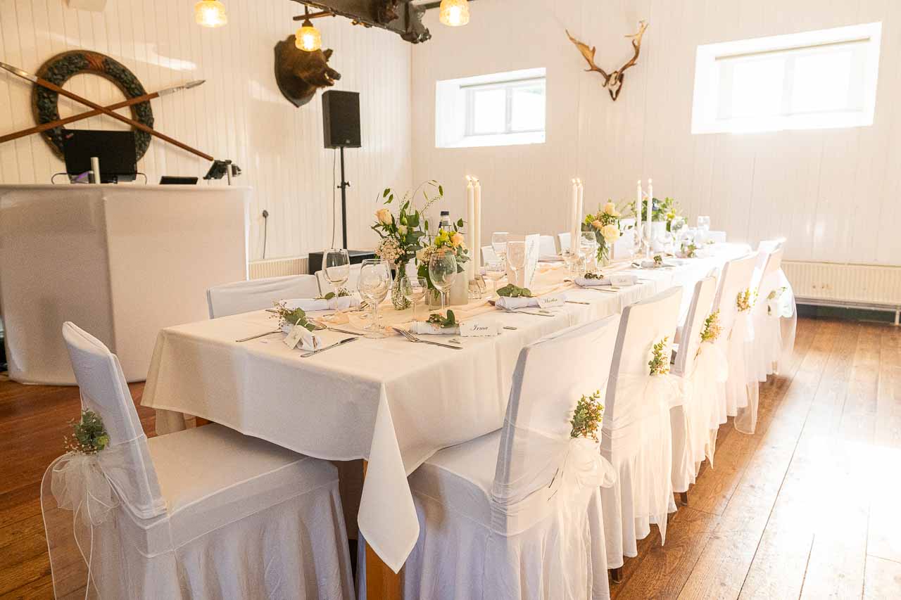 Festliche Hochzeitstafel mit weissen Stuehlen und Blumenschmuck. Romantische Dekoration fuer die Hochzeitsfeier in schoenem Ambiente.