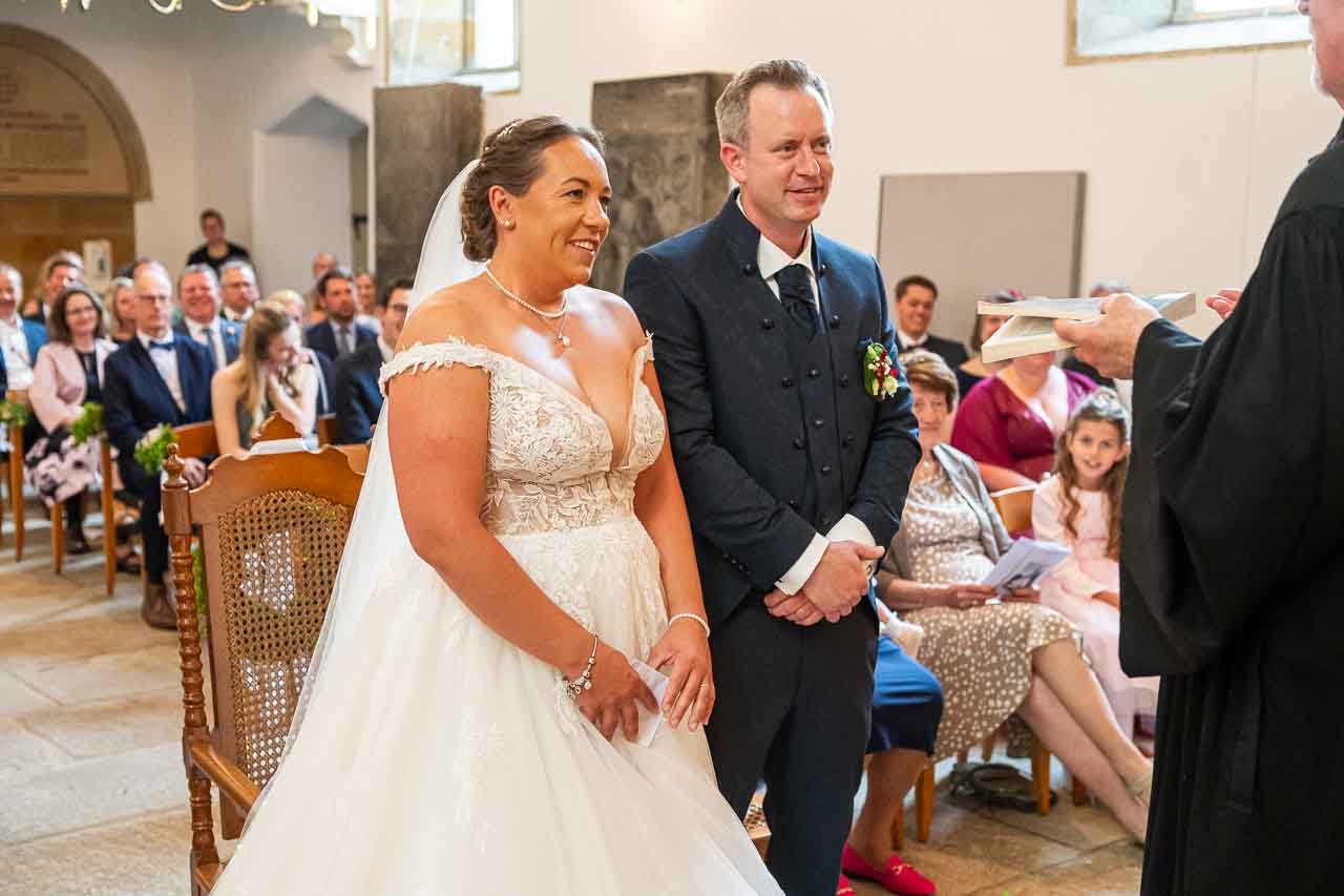 In der Kirche: Brautpaar sagt Ja-Wort. Die Braut im eleganten, schulterfreien Kleid, der Braeutigam im dunklen Anzug. Festliche Hochzeitsgesellschaft.