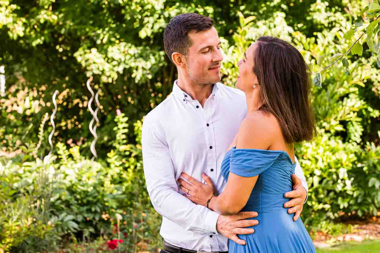 Verliebt in Mosterei Ockensen: Ein Paar in inniger Umarmung, sie im blauen Kleid, er im weißen Hemd, umgeben von üppigem Grün. Romantisch.