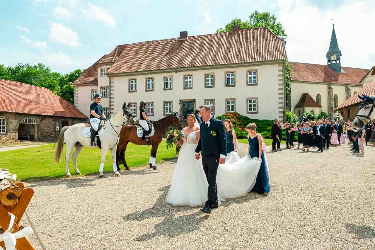 Hochzeit auf dem Schloss: Brautpaar schreitet mit eleganten Reitern und Gästen vor historischer Schlosskulisse. Romantische Hochzeitsfeier.