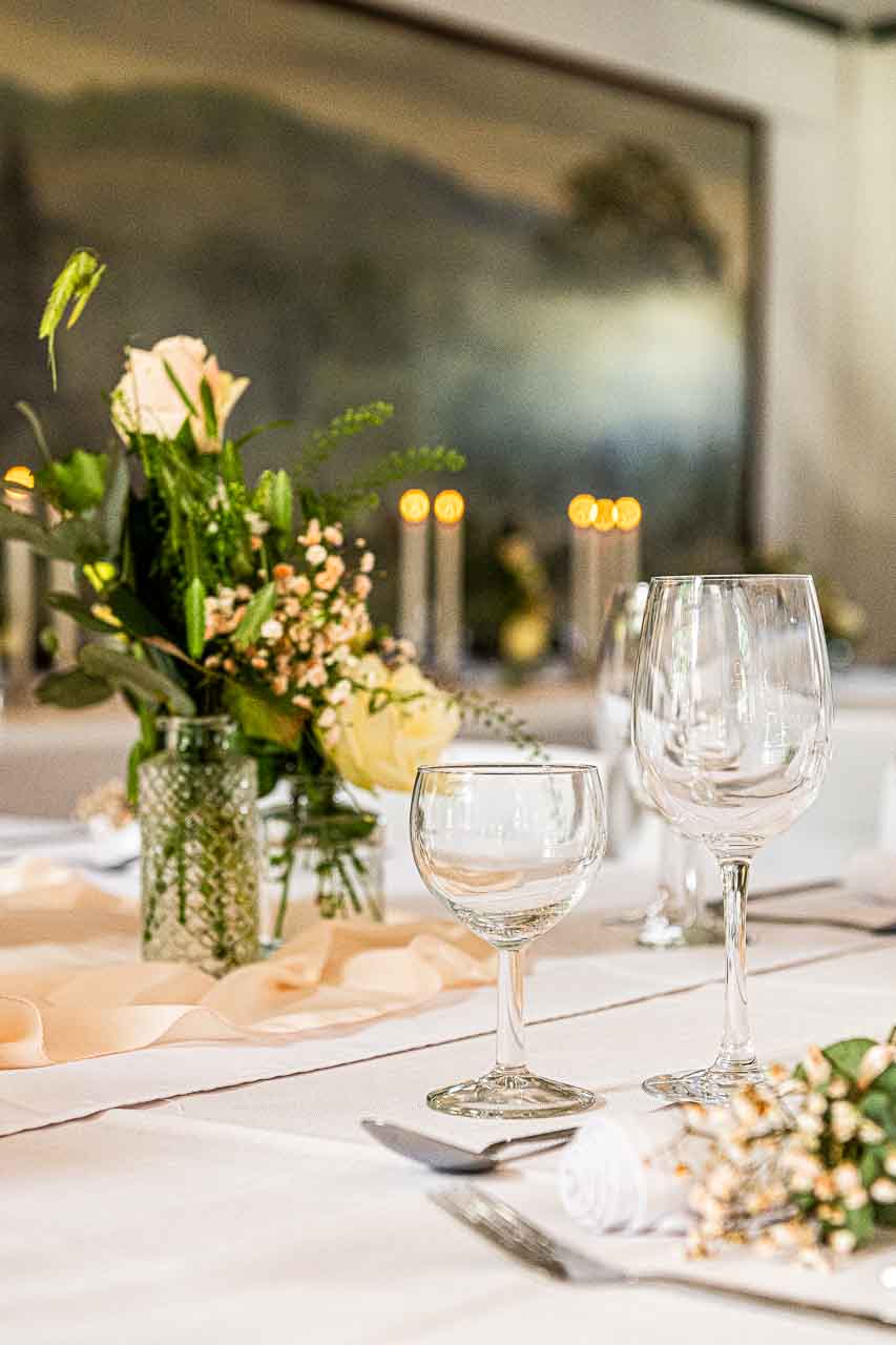 Elegante Tischdeko mit Rosen und zarten Blumen in Vasen, dazu stilvolle Glaeser und Kerzen. Romantische Atmosphaere fuer besondere Anlaesse.