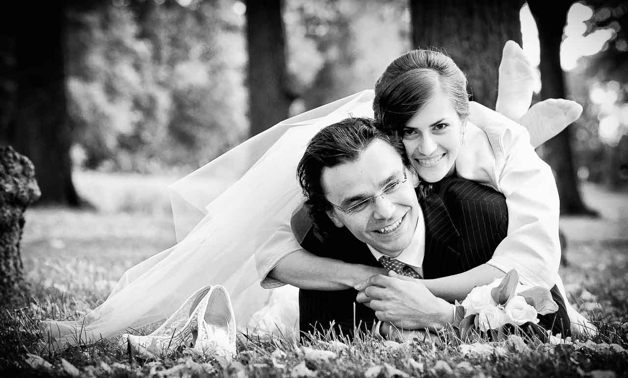 Schwarzweiß-Foto eines glücklichen Brautpaares im Park. Die Braut umarmt den Bräutigam, ihre Schuhe und der Brautstrauß liegen im Gras. Hochzeitsfotos Hannover Hildesheim