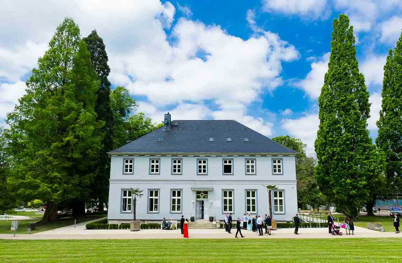Elegantes Herrenhaus mit Gaesten im Garten. Die Atmosphaere verspricht eine unvergessliche Feier in wunderschoener Umgebung. Festliche Momente im Freien.