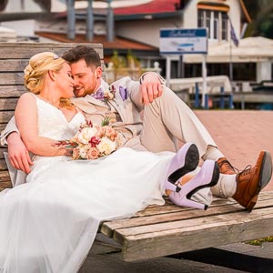 Ein verliebtes Brautpaar entspannt am Maschsee auf einer Bank. Die Braut im schoenen Kleid, der Braeutigam laessig. Romantische Hochzeit am Seeufer.