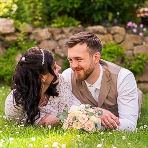Brautpaar liegt verliebt im gruenen Park auf einer Blumenwiese und schaut sich bei einer romantischen Hochzeit tief an