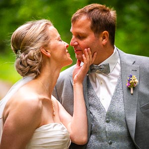 Brautpaar in liebevoller Pose im Park. Die Braut beruehrt zaertlich das Gesicht ihres Braeutigams an ihrem Hochzeitstag.