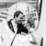Schwarzweiß-Foto: Glückliches Brautpaar im Oldtimer-Spiegelbild. Romantische Hochzeit, zarte Brautfrisur, lächelnder Bräutigam. Zeitlose Eleganz.