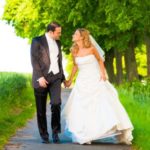 Romantische Hochzeit: Brautpaar Hand in Hand auf dem Weg ins Glück. Elegantes Brautkleid, stilvoller Anzug. Liebevolle Blicke im Grünen.