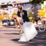 Romantische Hochzeit: Brautpaar tanzt verliebt auf der Straße. Die elegante Braut im weißen Kleid, der Bräutigam im Anzug. Glücksmomente für immer.