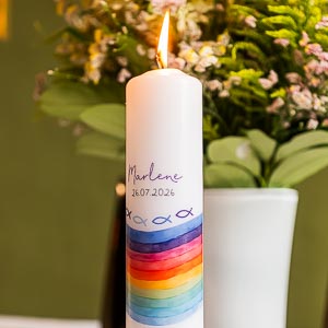 Eine festliche Taufkerze mit buntem Regenbogenmotiv und Namen Marlene vor einem Blumenstrauss fuer eine feierliche Zeremonie
