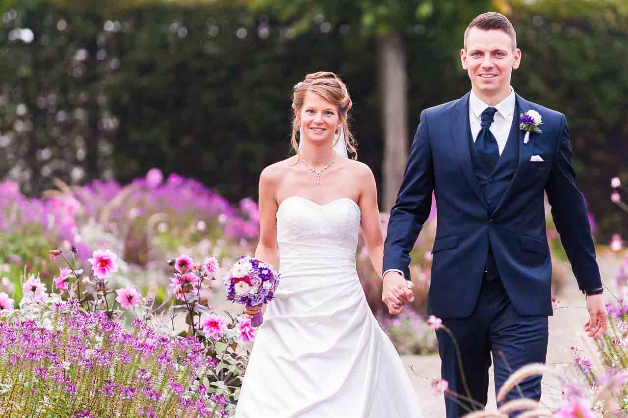 Ein strahlendes Brautpaar, Hand in Hand, in den Herrenhaeuser Gaerten in Isernhagen. Die Braut im weissen Kleid, der Braeutigam im eleganten Anzug.