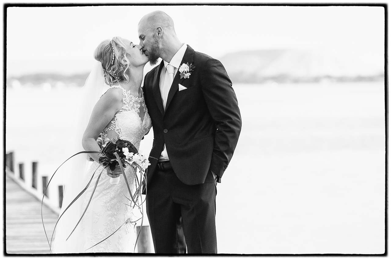 Ein zartes Schwarz-Weiss-Foto zeigt ein Brautpaar in Isernhagen, das sich liebevoll kuesst. Die Braut mit Schleier und der Braeutigam in elegantem Anzug.